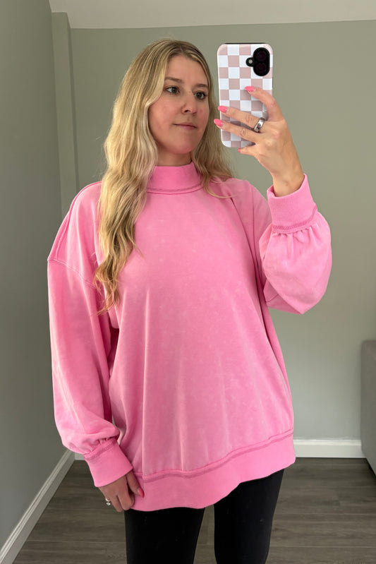 Person wearing a pink sweatshirt taking a mirror selfie in a room.