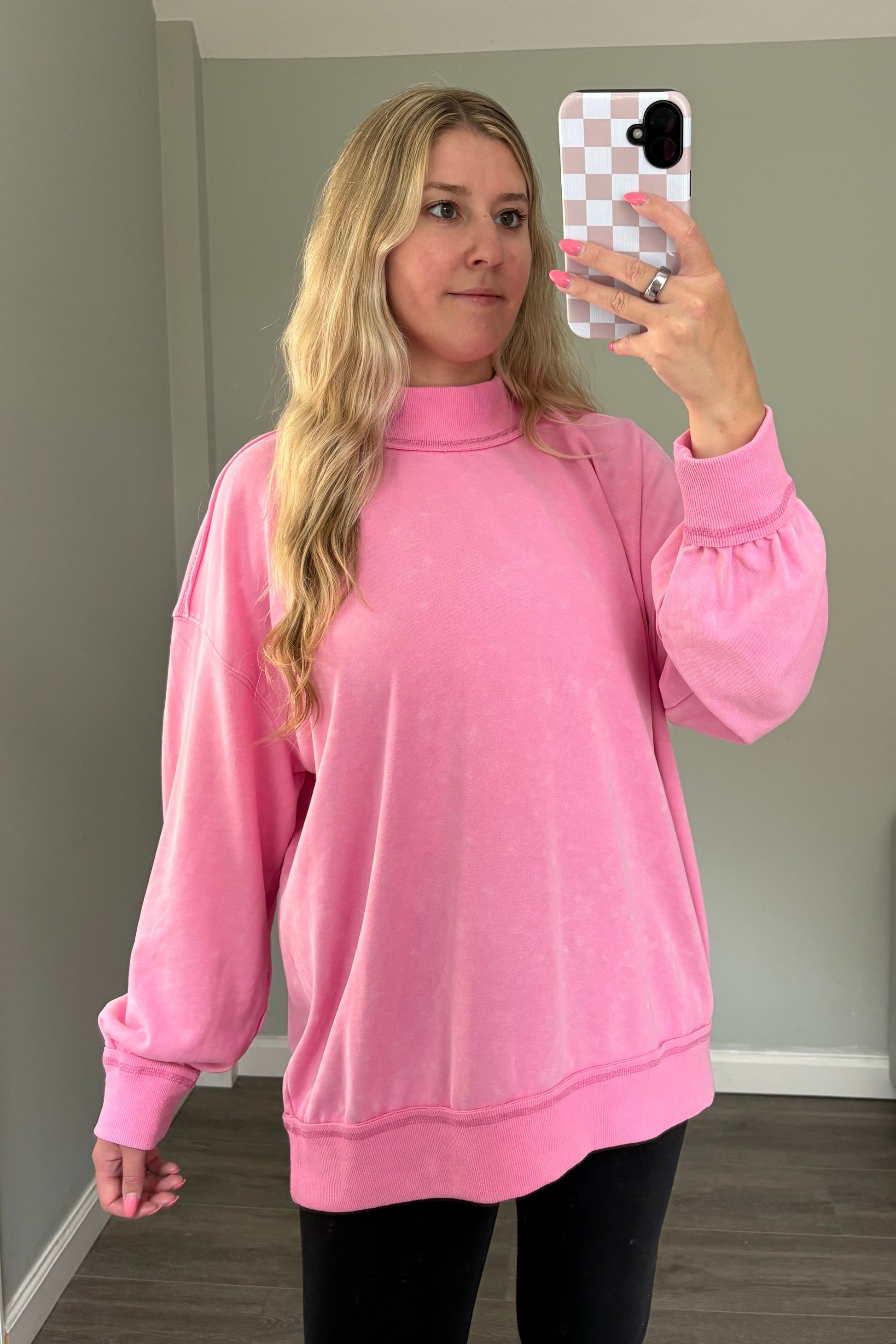 Person wearing a pink sweatshirt taking a mirror selfie in a room.