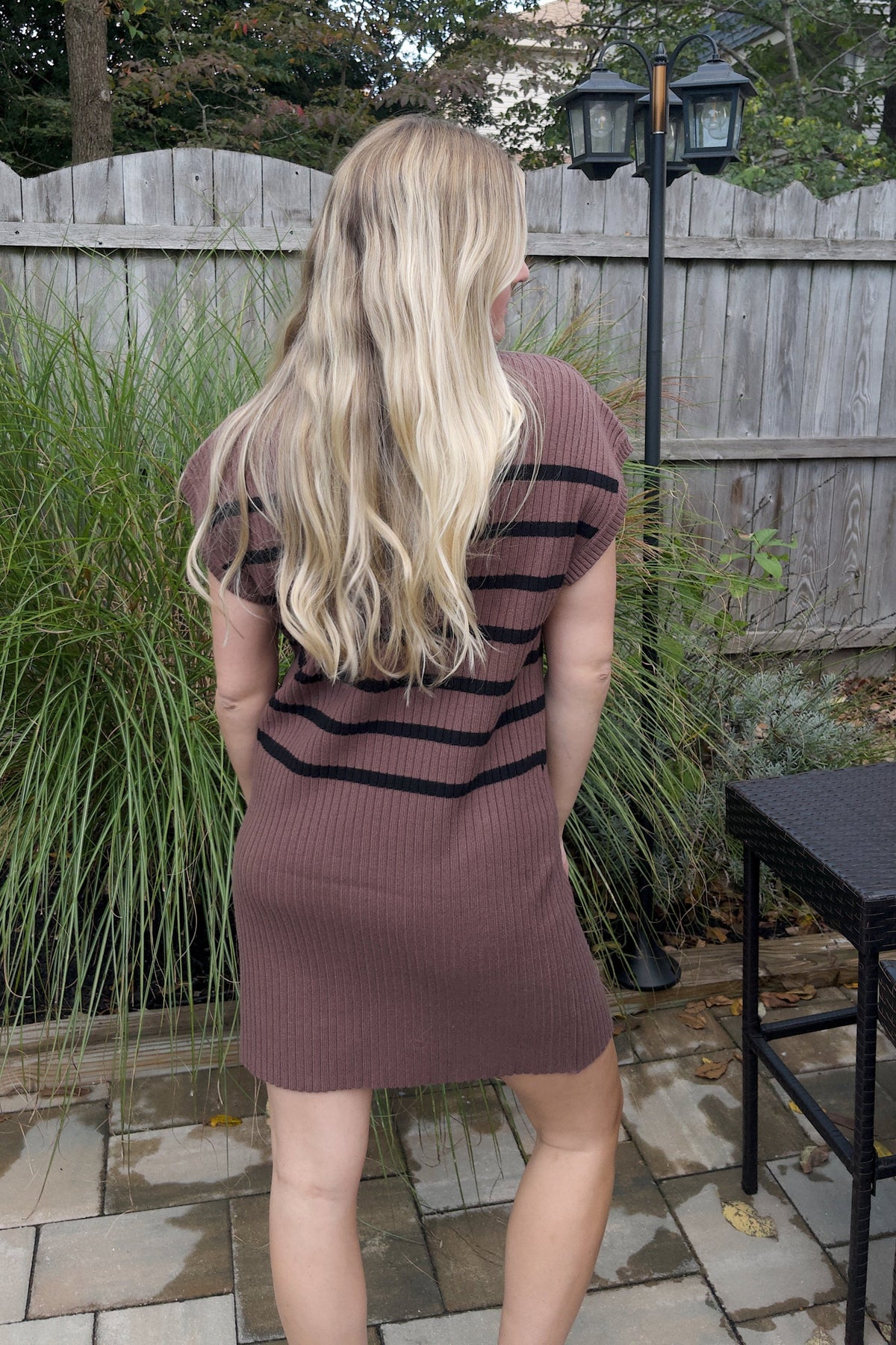 Back view of a brown ribbed sweater mini dress with black horizontal stripes and cap sleeves.