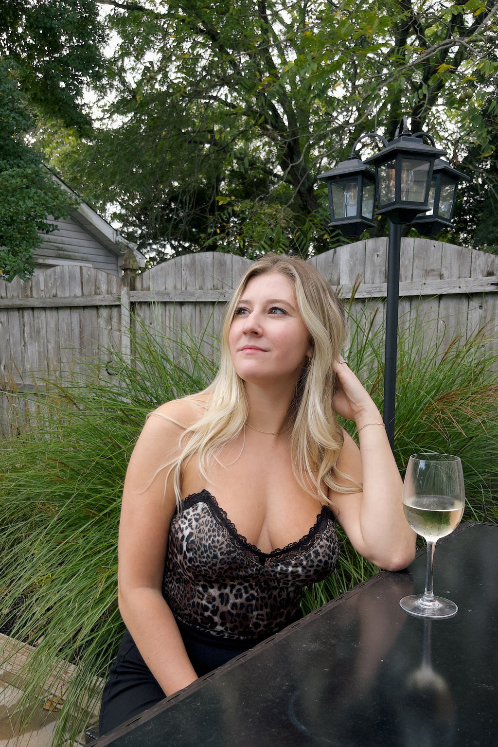 Model seated at an outdoor table wearing a cheetah print corset top with black lace trim and a deep V-neckline.

