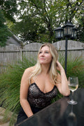 Model seated at an outdoor table wearing a cheetah print corset top with black lace trim and a deep V-neckline.

