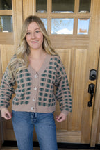 Model holding the hem of the Paige checkered cardigan to show its cropped length and ribbed waistband.

