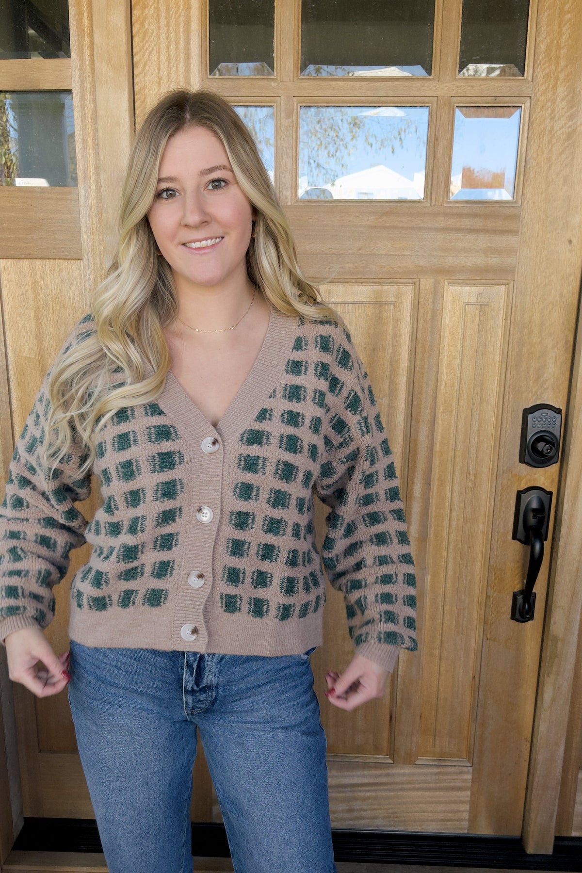 Model holding the hem of the Paige checkered cardigan to show its cropped length and ribbed waistband.

