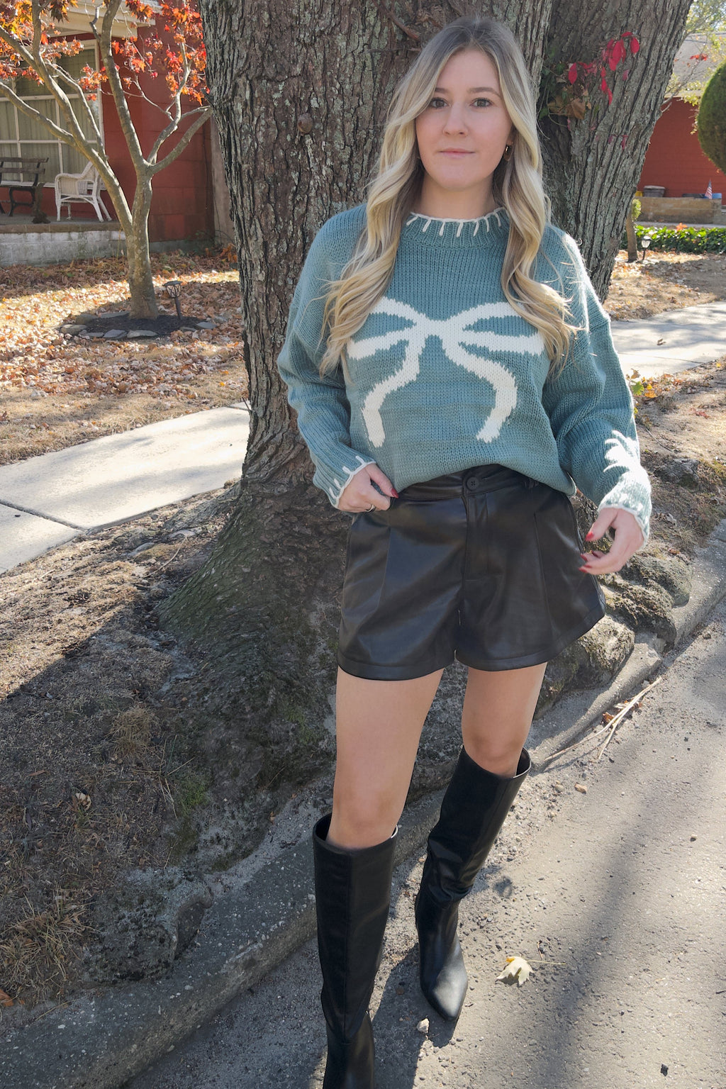 Front view of the Vivian blue knit sweater with a large cream bow graphic, styled tucked into black shorts.


