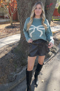 Front view of the Vivian blue knit sweater with a large cream bow graphic, styled tucked into black shorts.

