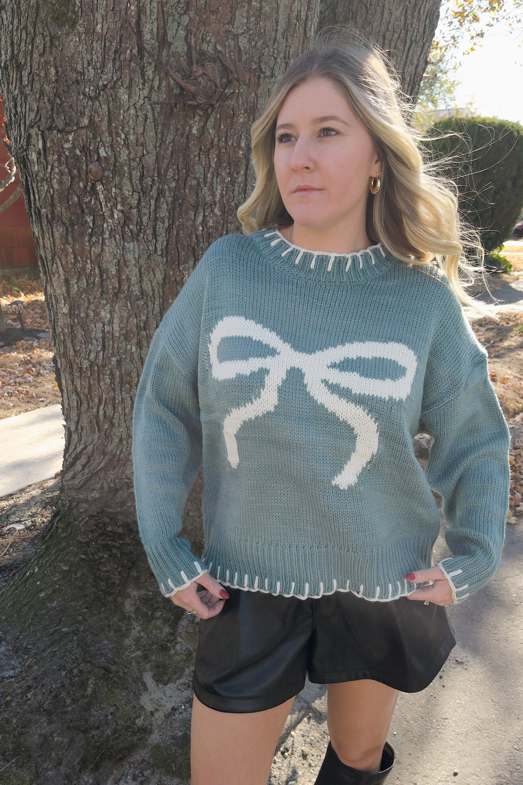 Vivian blue bow sweater shown untucked, with cream contrast stitching around the neckline, cuffs, and hem.

