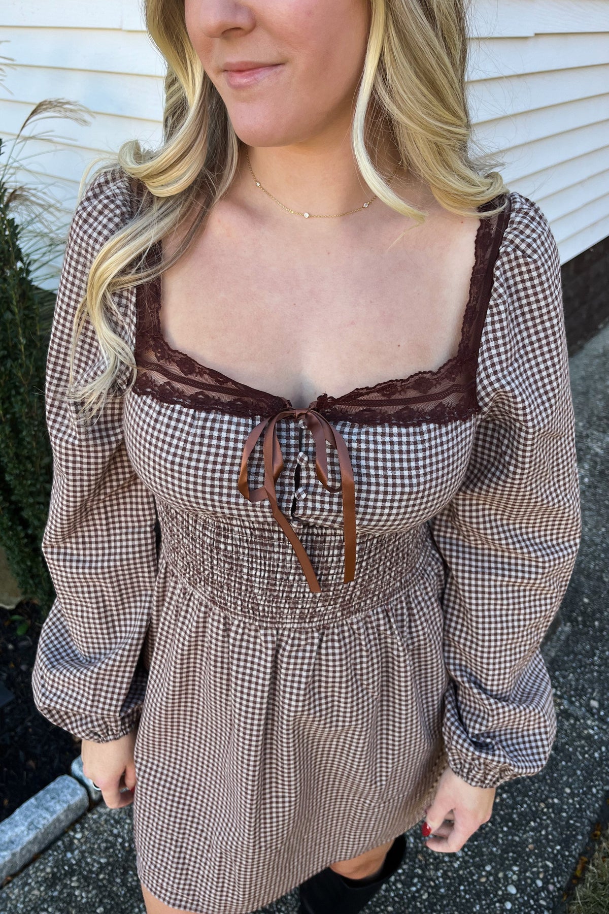 Close-up of the Harvest dress showing brown lace neckline trim, a ribbon bow, covered buttons, and smocked waist.


