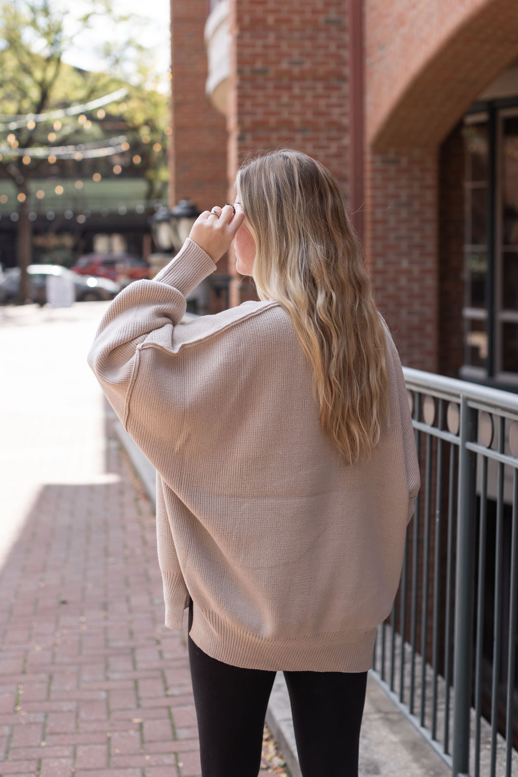 Angled back view of the sand beige knit sweater showing its roomy silhouette and dropped shoulders.

