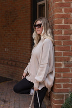 Sand beige oversized sweater showing dropped shoulders, long sleeves, ribbed cuffs, and a side-slit hem.

