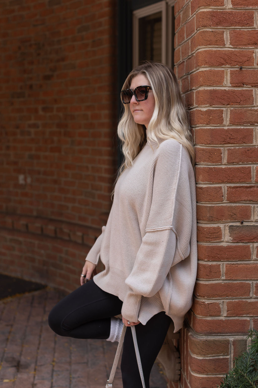 Sand beige oversized sweater showing dropped shoulders, long sleeves, ribbed cuffs, and a side-slit hem.


