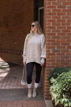 Full-length view of a model wearing the beige mock neck sweater with black leggings, cream socks, and ankle boots.

