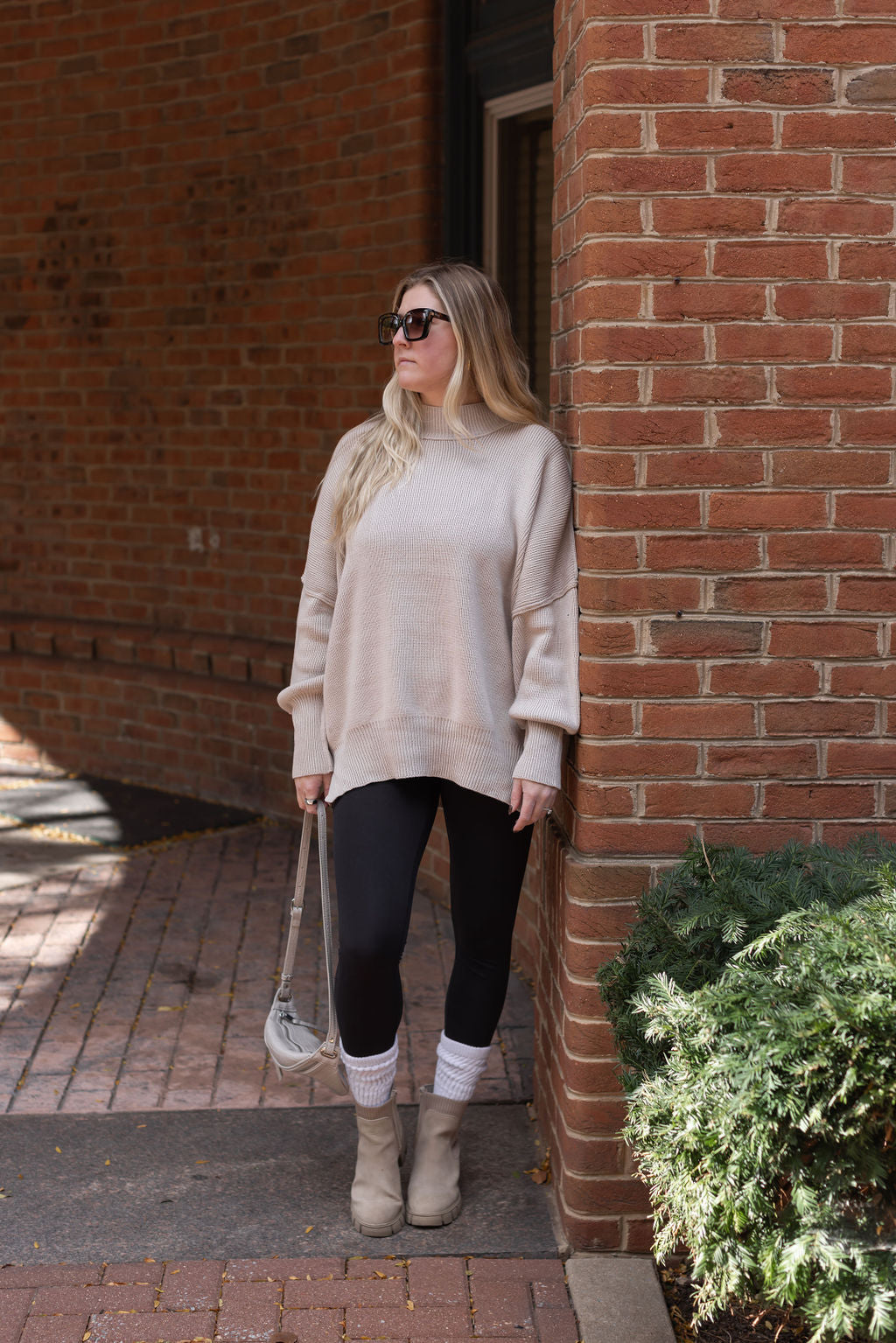 Full-length view of a model wearing the beige mock neck sweater with black leggings, cream socks, and ankle boots.

