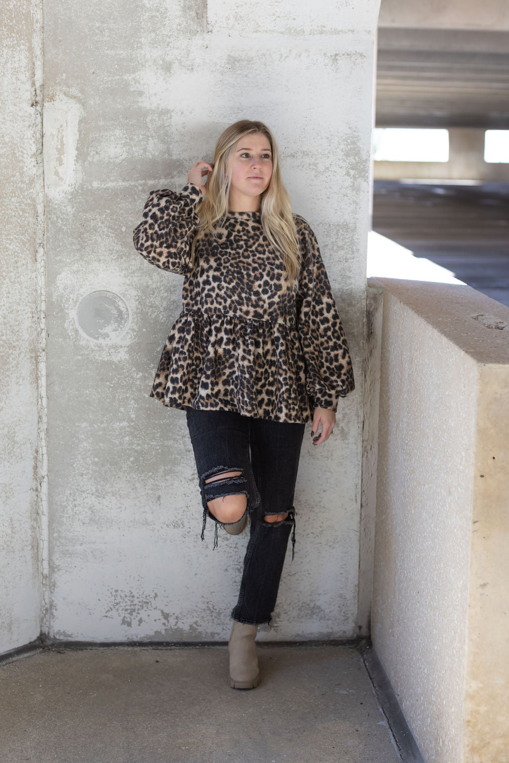 Full-length view of the Bianca leopard print top styled with ripped black jeans and beige ankle boots.

