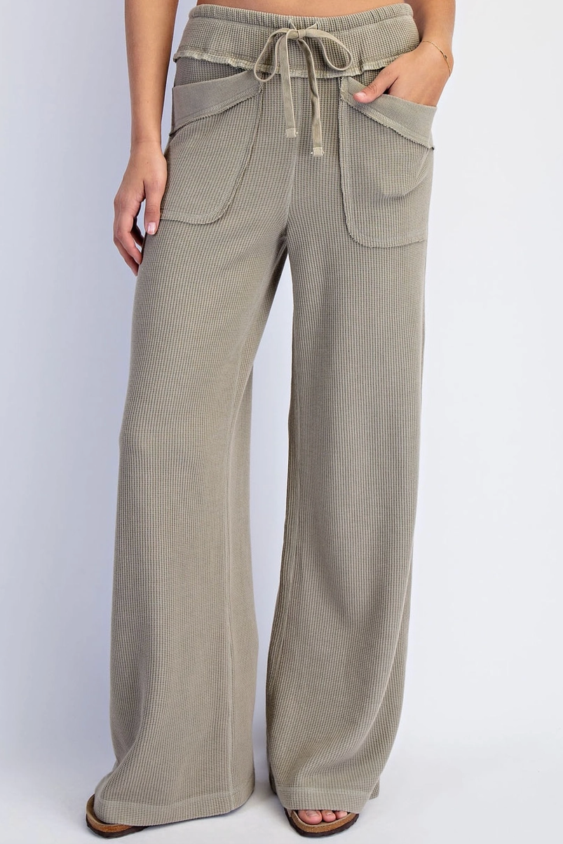 A person wearing wide-leg drawstring pants in a light taupe-beige color, shown from the waist down against a plain light gray studio background.