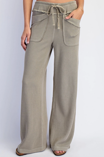 A person wearing wide-leg drawstring pants in a light taupe-beige color, shown from the waist down against a plain light gray studio background.