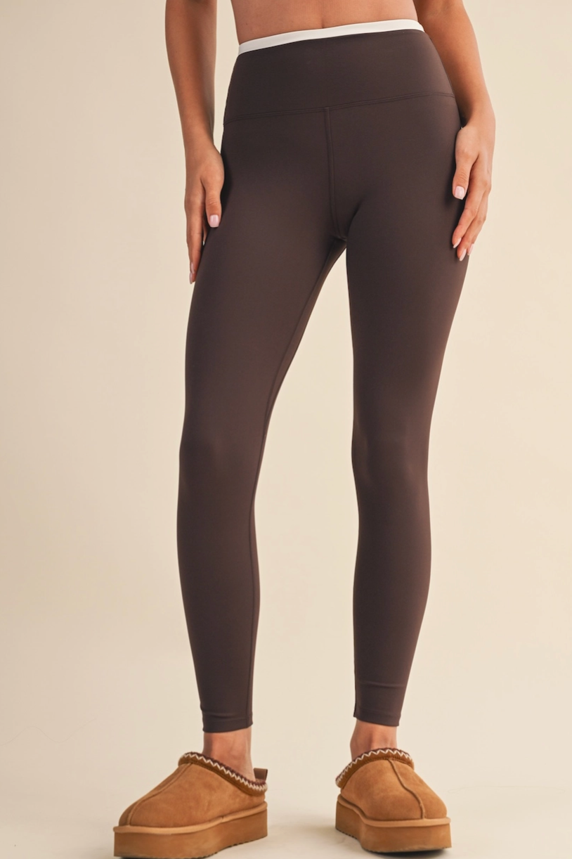 A model from the waist down wearing dark brown high-waisted leggings and tan platform slippers against a solid beige studio background.