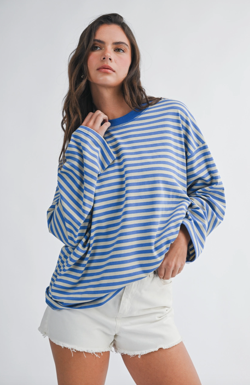 A woman modeling a blue and white striped long-sleeve t-shirt with white frayed denim shorts, posed against a light gray studio background.