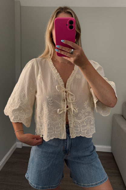 Person wearing a lace top and denim shorts holding a pink phone.