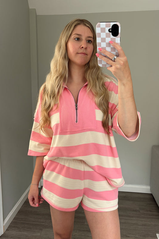 Woman taking a mirror selfie wearing a pink and white striped outfit in a room.