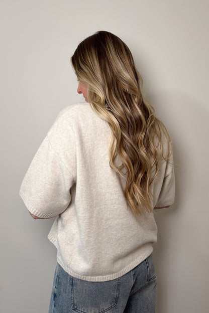 Person wearing a beige sweater and blue jeans against a plain background