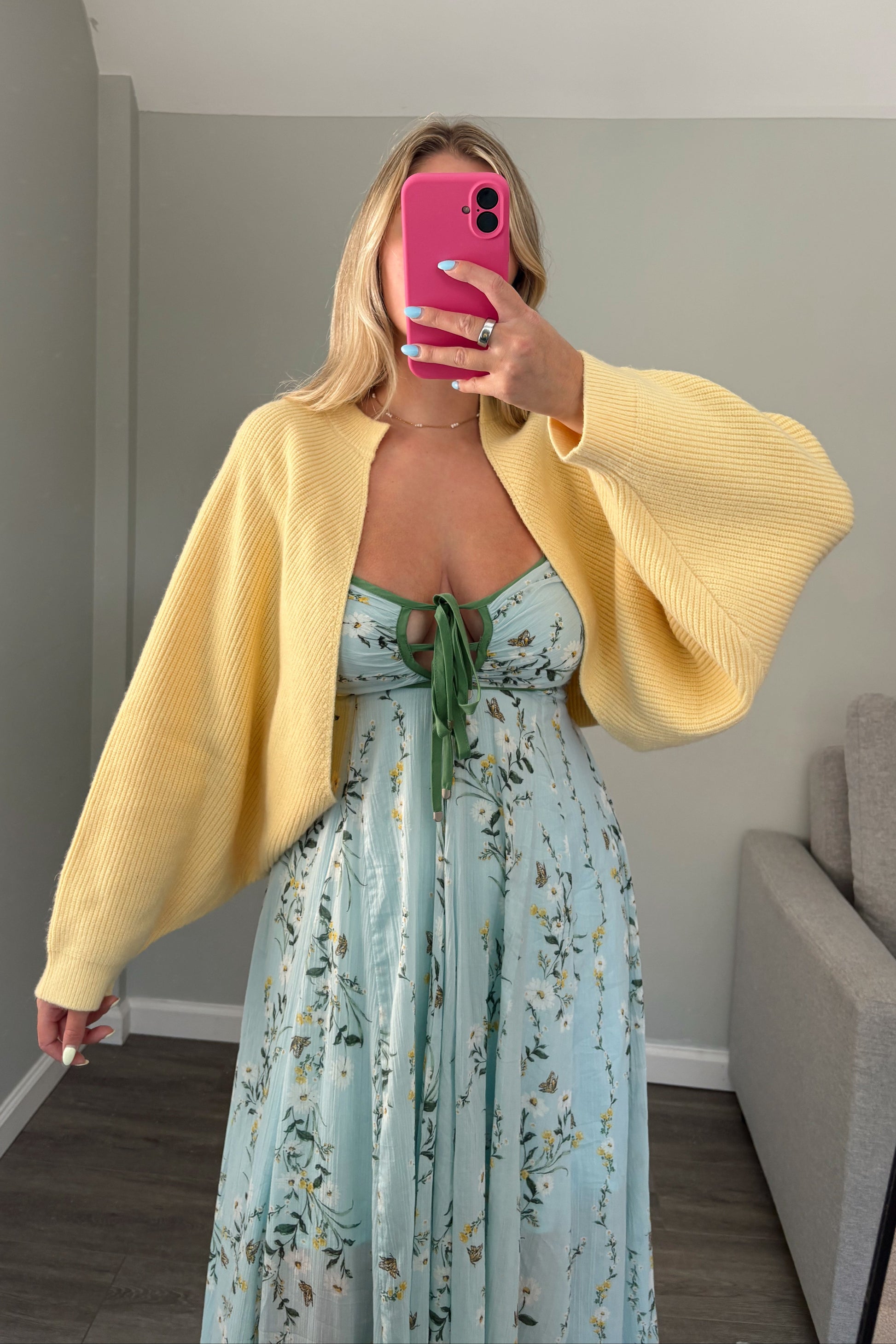 Person wearing a yellow cardigan and floral dress, holding a pink phone.