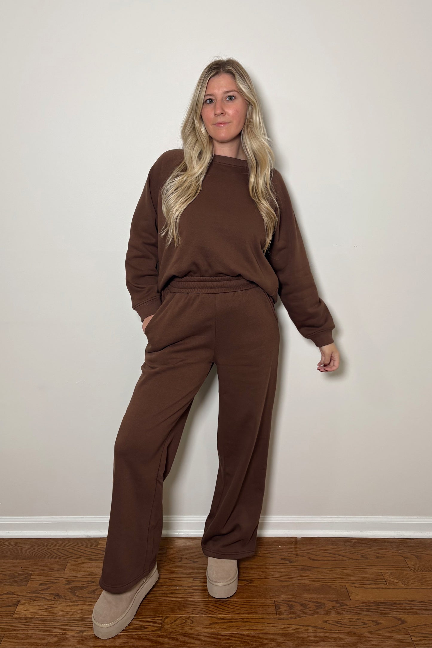 Person wearing a brown sweat set/lounge set standing against a plain wall.