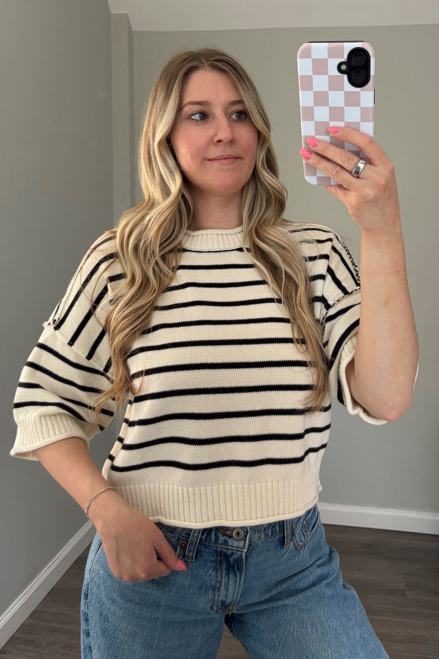 Woman taking a mirror selfie wearing a striped sweater and jeans.