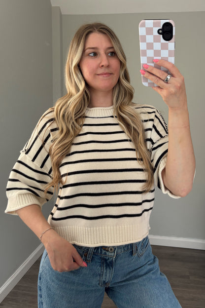 Woman taking a mirror selfie wearing a striped sweater and jeans.