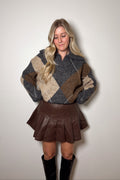 Harper brown faux leather pleated mini skirt styled with an argyle sweater and tall black boots.

