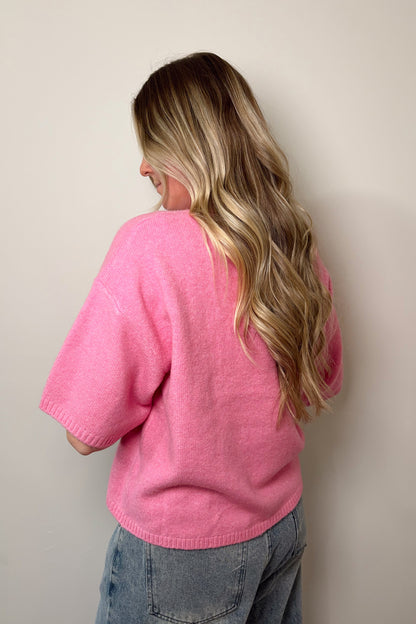 Person wearing a pink sweater and blue jeans against a plain background
