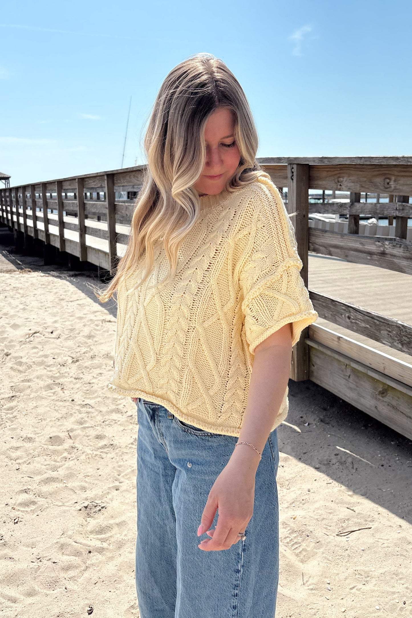 Person wearing a yellow top and blue jeans standing on a sandy beach.
