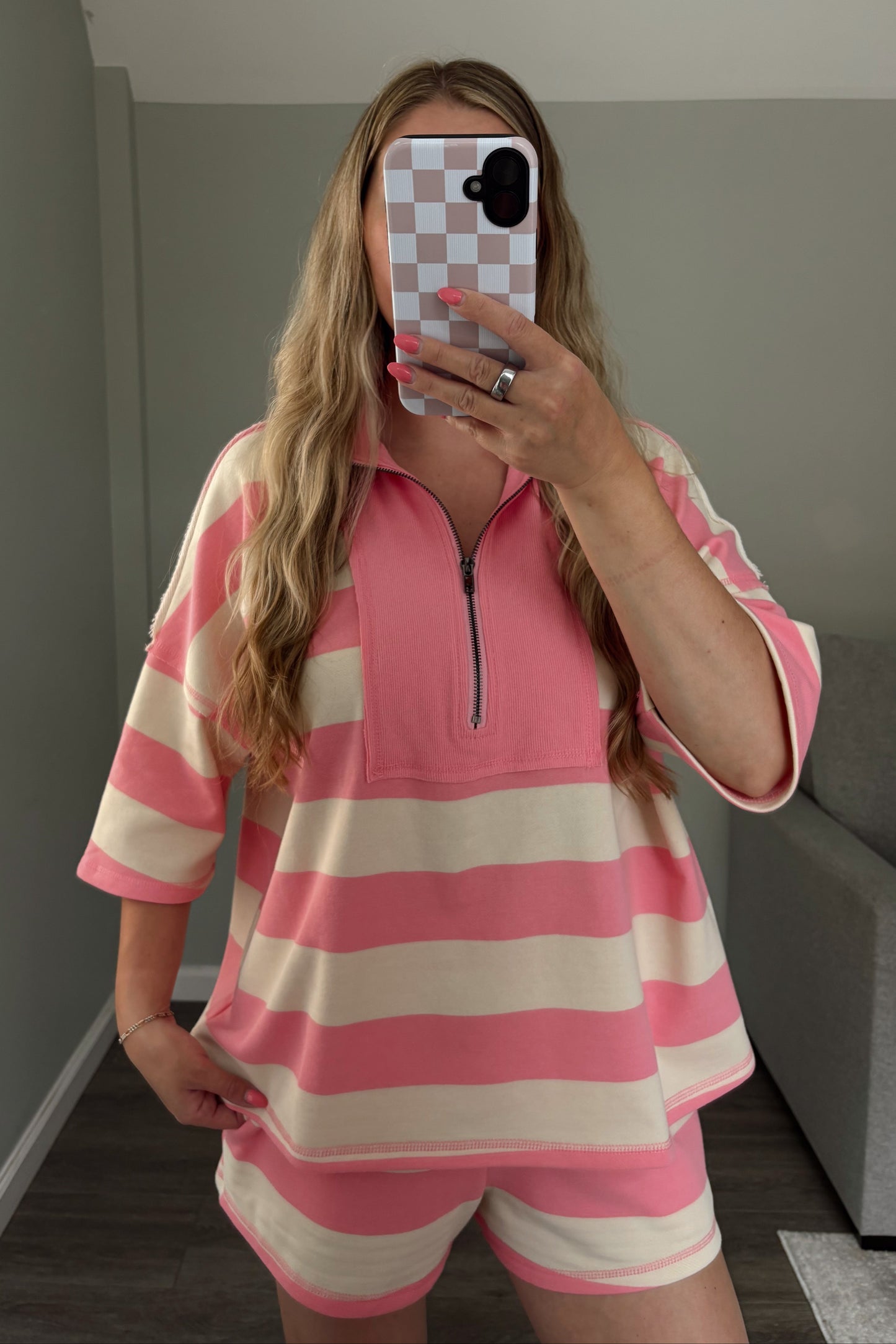 Person wearing a pink and white striped outfit taking a mirror selfie.