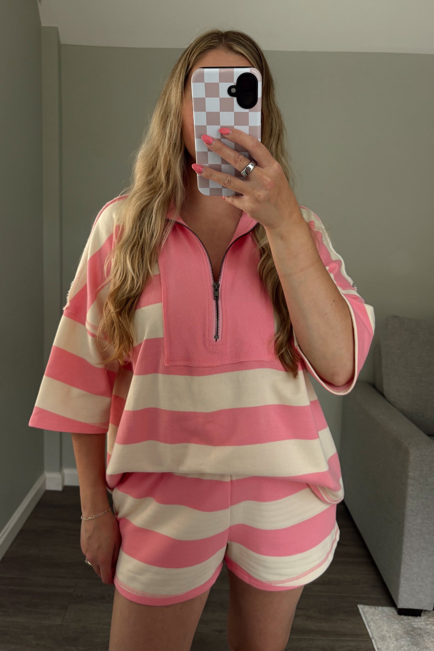 Person wearing a pink and beige striped outfit taking a mirror selfie.