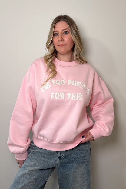 Person wearing a pink sweatshirt with "I'm too pretty for this" text, standing against a plain background