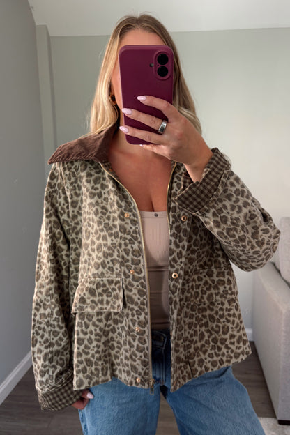 A woman takes a mirror selfie wearing a leopard print button-up jacket with a brown sherpa collar, paired with a beige top and blue jeans in a home setting.