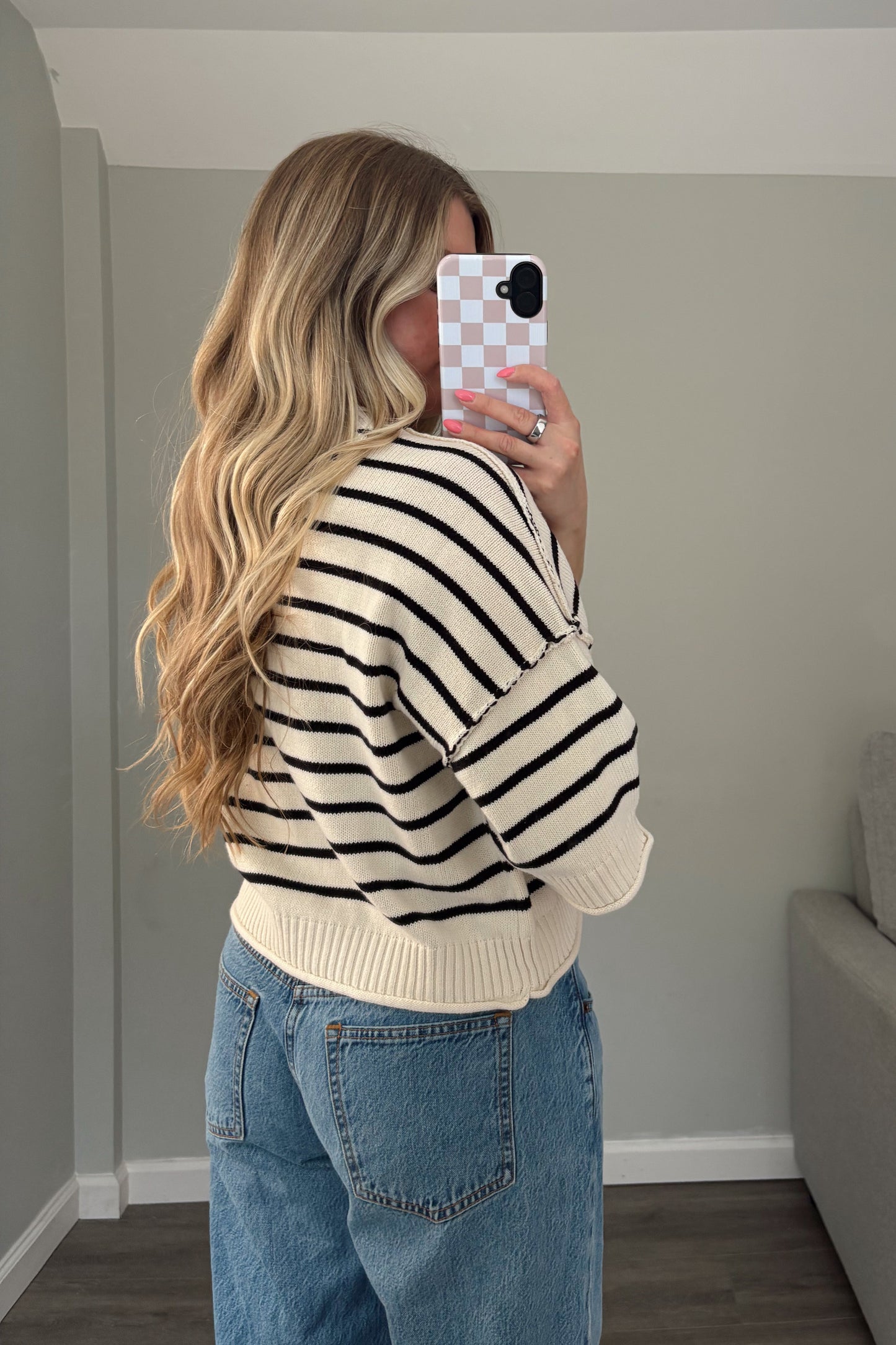 Person wearing a striped sweater and jeans taking a mirror selfie.