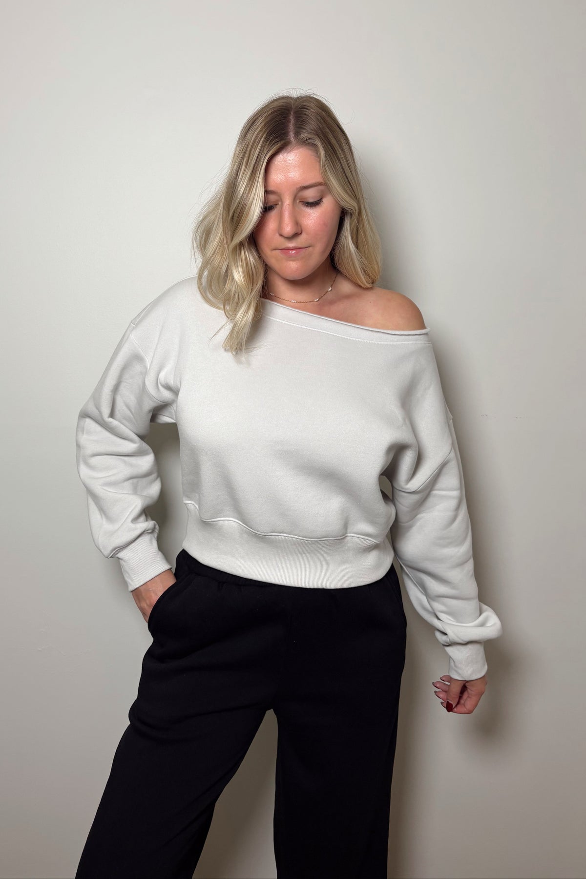 Front view of the Haven stone fleece pullover worn off one shoulder, showing its cropped hem above black pants.

