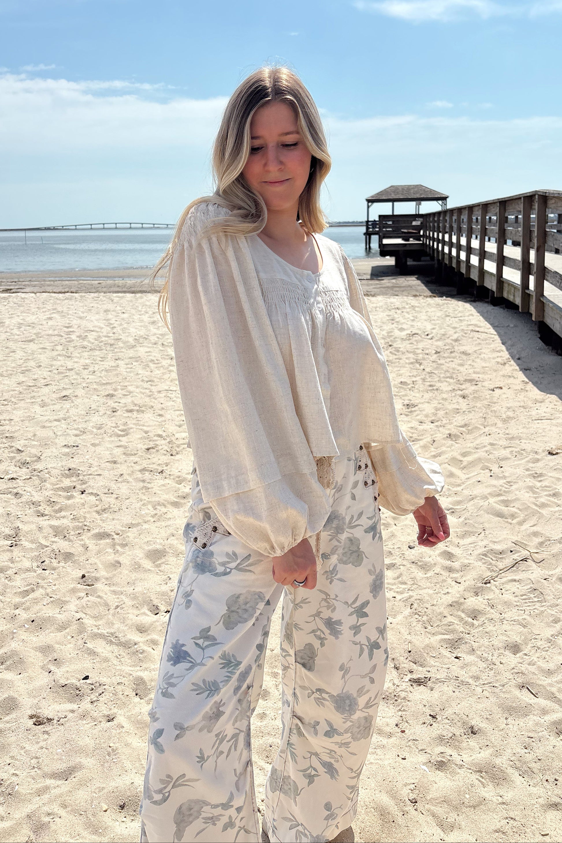 Person wearing a white shirt with floral patterned pants on a beach.