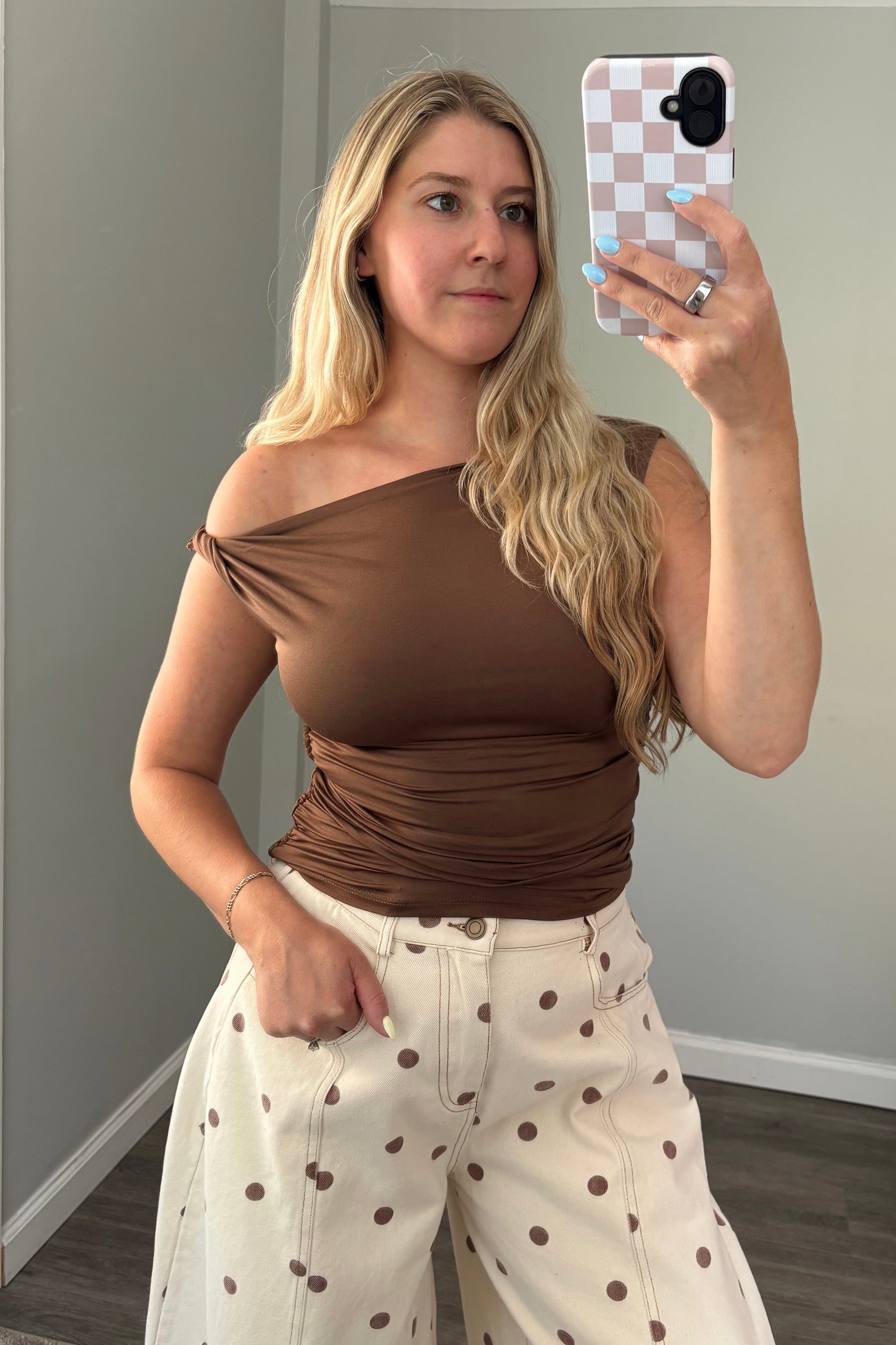 Woman taking a mirror selfie wearing a brown top and white pants with brown polka dots.