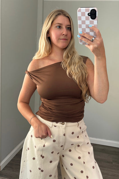 Woman taking a mirror selfie wearing a brown top and white pants with brown polka dots.