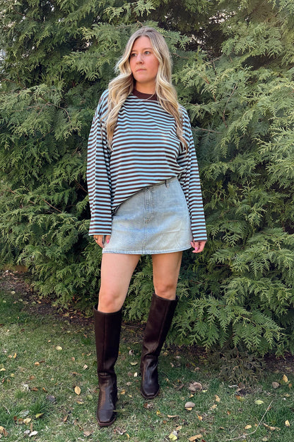 Person standing outdoors on a grassy area with trees in the background