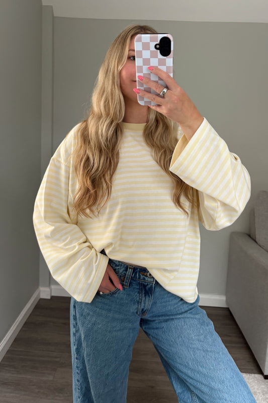 Person wearing a yellow and white striped top and blue jeans taking a mirror selfie.