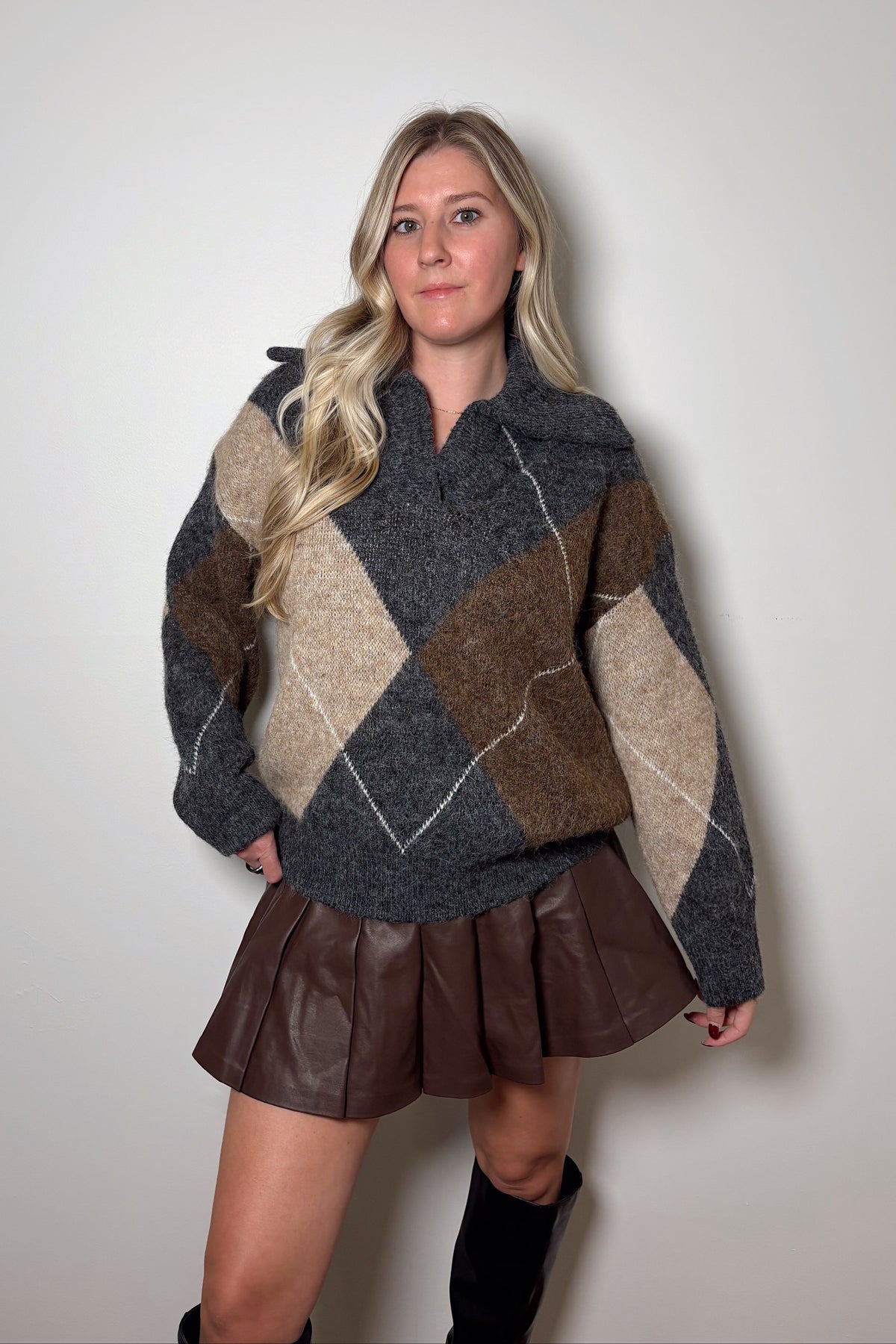 Blake collared sweater showing its large neutral-tone argyle pattern and dropped shoulders, styled with a brown mini skirt.


