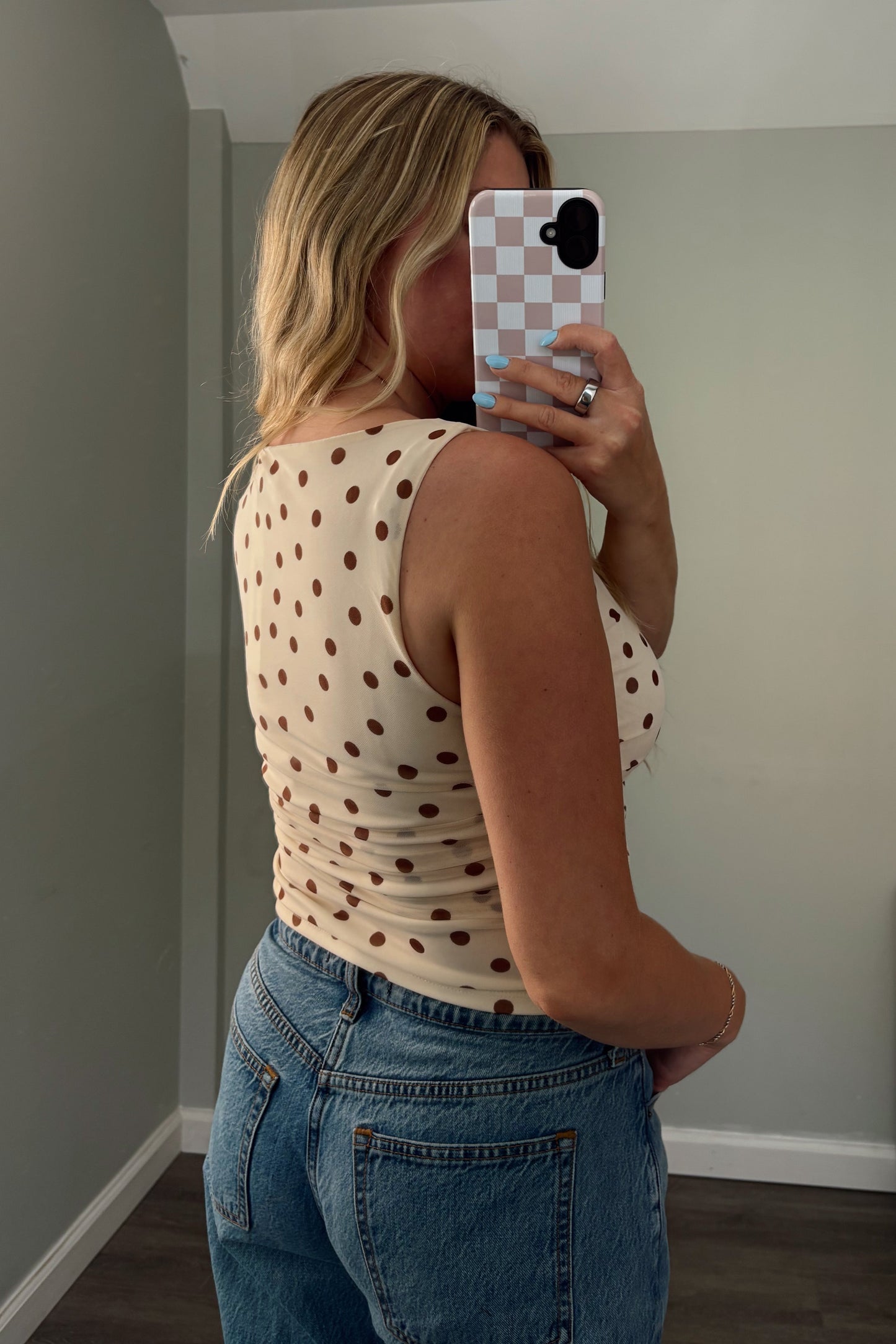 Person taking a mirror selfie wearing a polka dot top and jeans in a room.