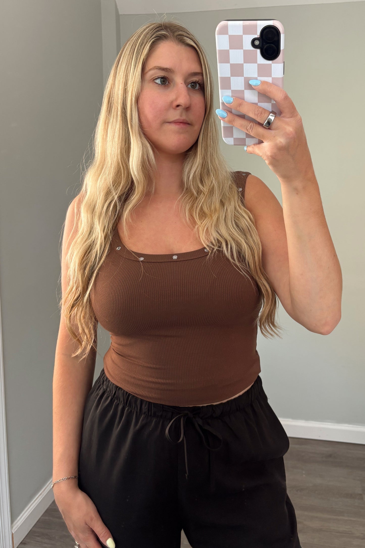 Woman taking a mirror selfie wearing a brown top and black pants in a room with a gray couch.