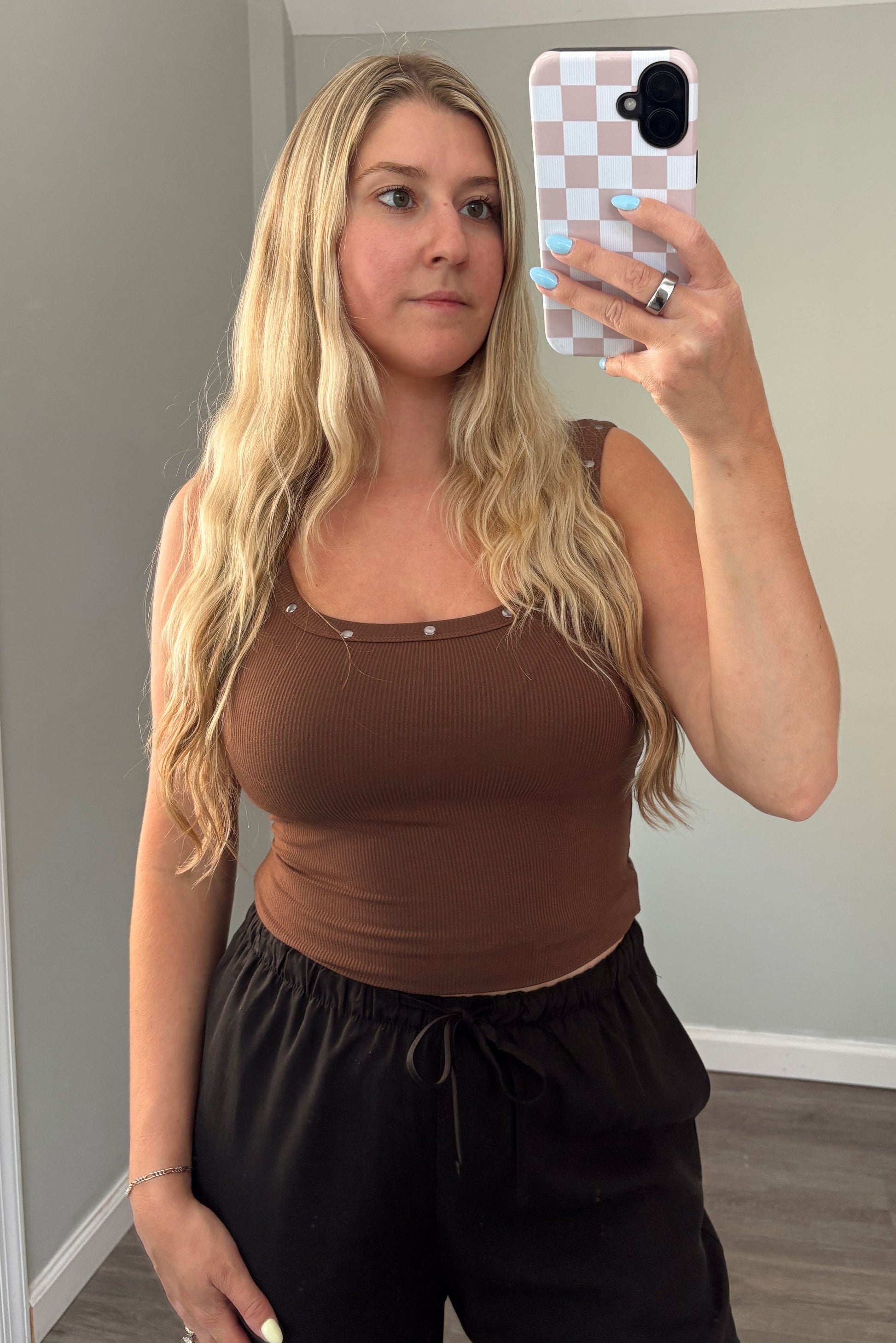 Woman taking a mirror selfie wearing a brown top and black pants in a room with a gray couch.
