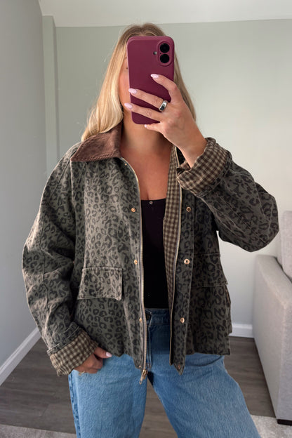 A woman takes a mirror selfie wearing a brown and black leopard print jacket with a brown gingham lining and collar, paired with blue jeans and a black top.