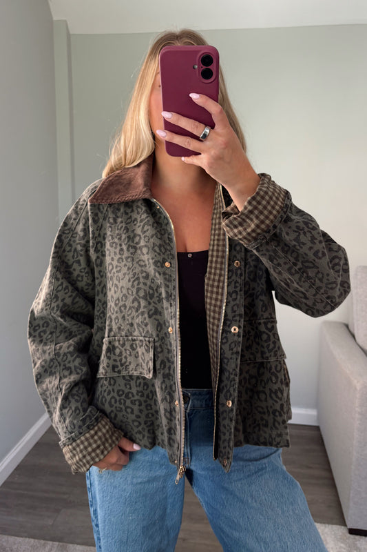 A woman takes a mirror selfie wearing a brown and black leopard print jacket with a brown gingham lining and collar, paired with blue jeans and a black top.