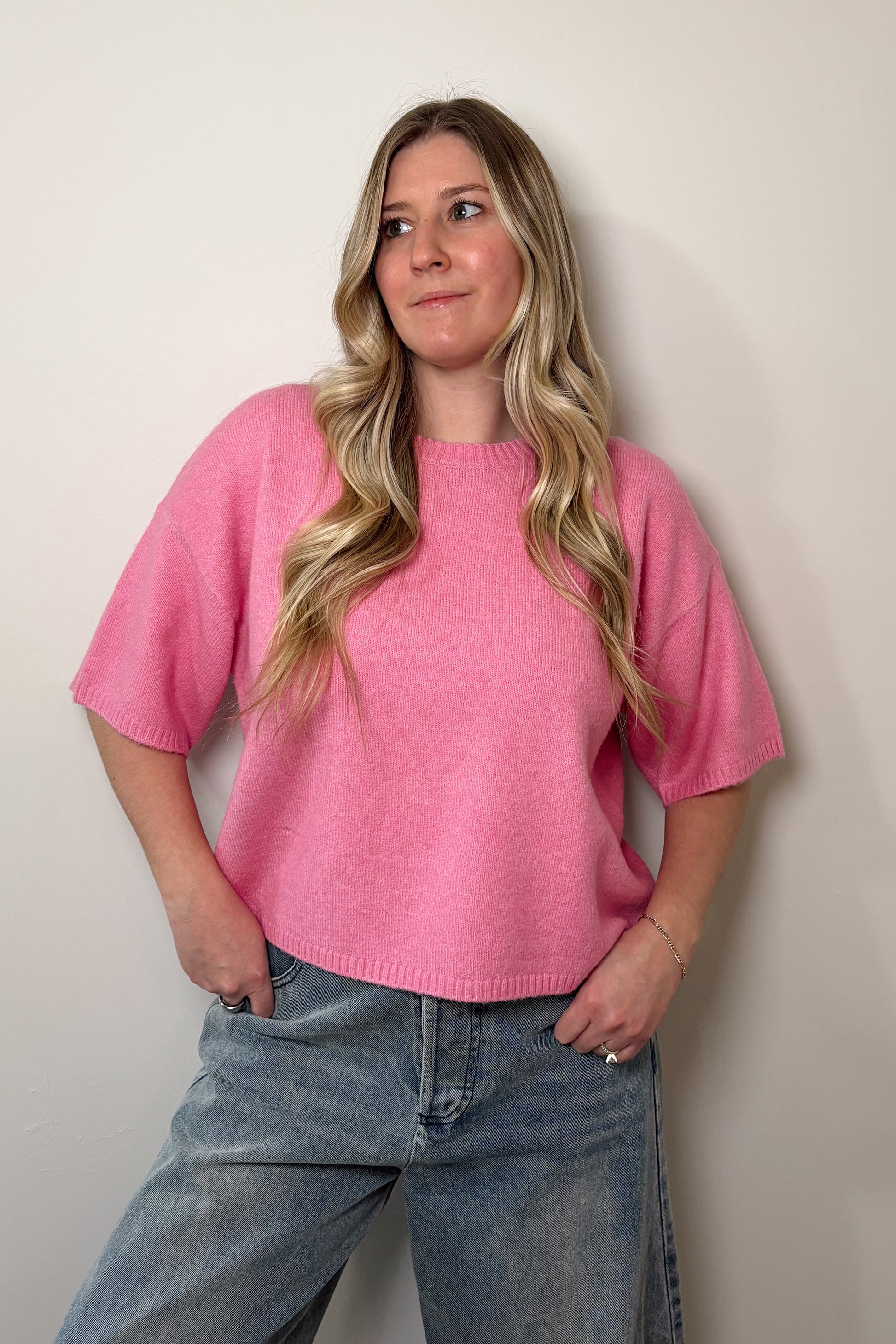 Woman wearing a pink sweater and blue jeans against a plain background