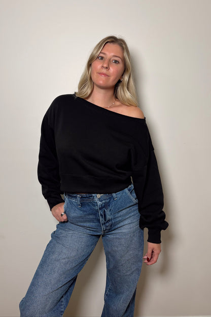 Woman wearing a black off-shoulder top and blue jeans against a plain background